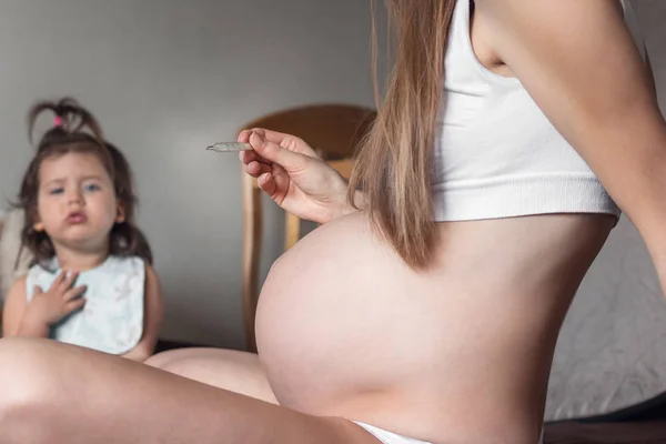 Una joven embarazada con un largo cabello rubio 32, 33 semanas de plazo mide la temperatura corporal y mira el termómetro — Foto de Stock