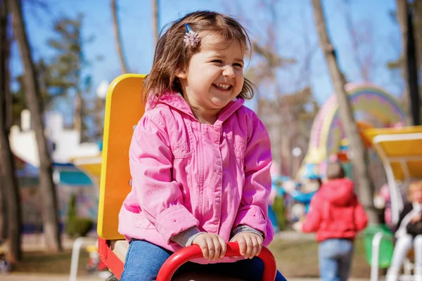 Mała dziewczynka jazda na huśtawce i uśmiech i zabawy na placu zabaw — Zdjęcie stockowe