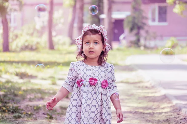 Beautiful Caucasian little girl, has happy fun cheerful smiling face, white dress, soap bubble blower. Portrait nature. Stock Picture