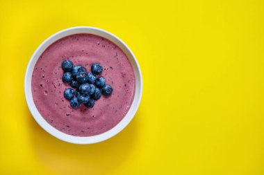 Sarı arka planda yaban mersini ve muz ile yumuşatıcı kase, vegan, organik, yassı, kopyalanmış