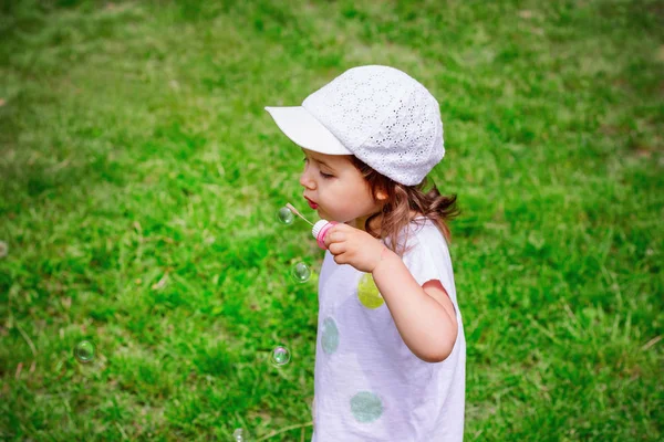 A little girl blowing soap bubbles in summer park. — Stock Photo, Image