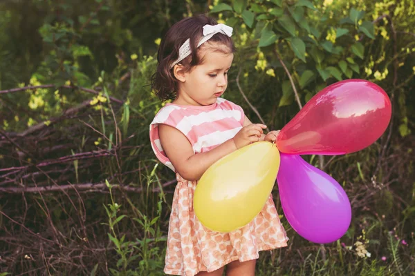 Une petite fille de 3, 4 ans en robe rose blanche est heureuse et rit et tient des ballons — Photo