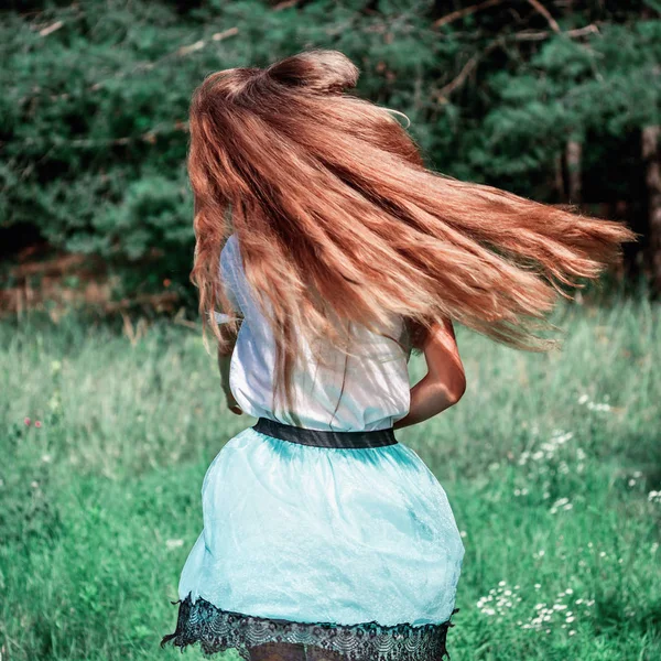 Uma adolescente em uma saia e uma blusa branca salta, acenando longos cabelos loiros ao ar livre, em um tom de moda — Fotografia de Stock
