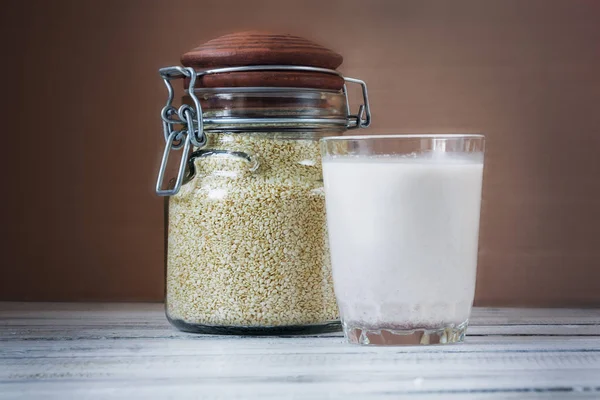 Leite de semente de gergelim em um copo. Sementes de sésamo branco em uma mesa. Dieta alimentar crua . — Fotografia de Stock
