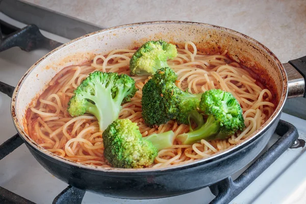 Preparation of spaghetti in a frying pan on a stove with broccoli and tomato sauce — Stock Photo, Image