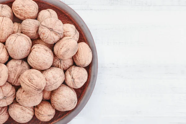 stock image whole walnuts in a clay plate on a white wooden background. Rustic style.