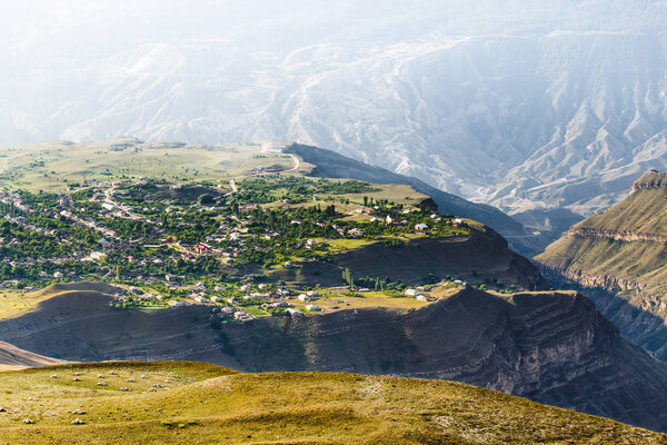 Fantastic highland village Novyy Argvani placed on a green plateau and surrounded by canyon and Caucasus Mountains. Sunny landscape with haze on background in the morning. Dagestan Republic, Russia