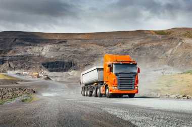 Modern orange european truck with white heavy duty dump trailer drives after load from quarry in a sunny day clipart