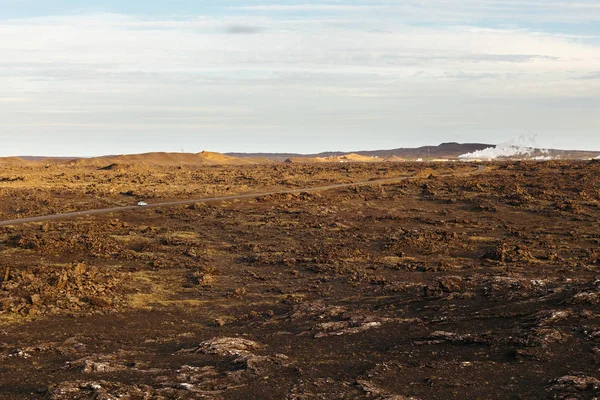 Exploring geothermal energy. Road to geothermal power plant with steam in desolate volcanic landscape with cloudy sky on a sunny summer evening. Road trip at Reykjanes Peninsula, Iceland