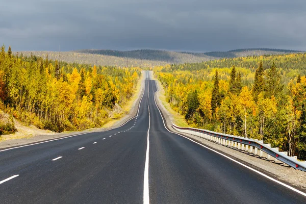 Yol ileri. Düz boş asfalt yol, tepeler, renkli sonbahar orman ve bulutlu gökyüzü güneşli bir günde. Tayga ormanı manzara. Kuzeye yolculuk. Kola Yarımadası, Murmansk bölgesi, Rusya Federasyonu