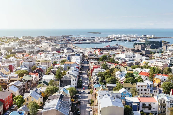 Rahat şehir komşuluktaki yeşil ağaçlar, düz sokak ve açık güneşli yaz günü limanda deniz ile panoramik görünümü yukarıdaki. Reykjavik, İzlanda