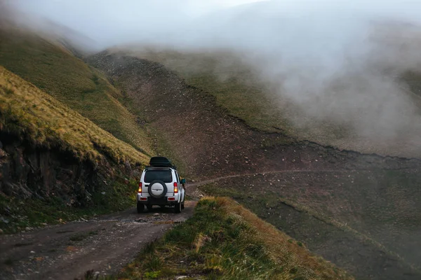 Gümüş off-road araç dağlarında yolculuğa. Kompakt Suv, siste sarp dağ tarafı dar tehlikeli yol yokuş yukarı gidiyor. Kafkas Dağları