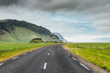 Bir bulutlu yaz gününde güzel yeşil alanlar ve rocky Dağları arasında kırsal kesimde asfalt yol. Çevre yolu sayısı 1 İzlanda'daki seyahat