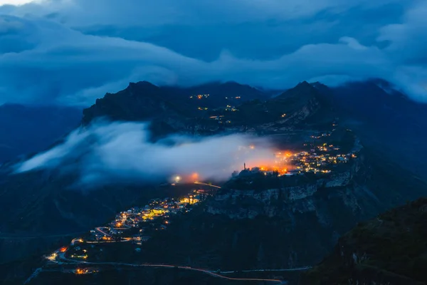 Gunib dağ köyü gece renkli aydınlatma ile bulutlar yayla bir plato üzerinde. Popüler turistik yerde uzun pozlama ile manzara. Kafkas Dağları, Dağıstan Cumhuriyeti, Rusya Federasyonu