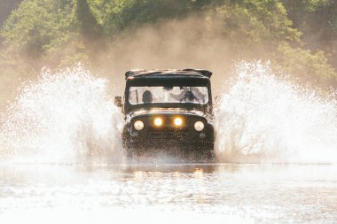 Eski klasik 4x4 araba sıcak güneşli bir günde güzel sıçramaları ile su geçiş, düşük açı ön görünüm. Ormanda aşırı off-road turu