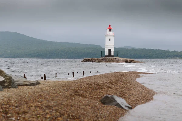 Deniz feneri Tokarevsky çakıl taşı sahilinde ve dalgalar Vladivostok şehrinde bulutlu bir günde. Japon Denizi kıyısında mimari görüşü. Primorsky Krai, Uzak Doğu, Rusya.
