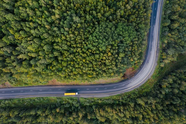 Yeşil orman ağaçları arasındaki dağ yolu eğrisinin yukarıdan aşağıya doğru görüntüsü. Otobanda kargo karavanı olan yarı kamyon. Kopya alanı ile ulaşım ve doğal manzara arkaplanı