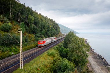 Baykal Gölü kıyısındaki Trans-Sibirya Demiryolu 'ndaki yeşil orman ağaçları ve bulutlu gökyüzü taşıyan yük treni. Buryatia, Sibirya, Rusya 'daki Doğu Sibirya Demiryolu