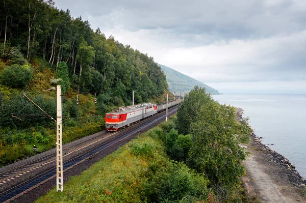 Baykal Gölü kıyısındaki Trans-Sibirya Demiryolu 'ndaki yeşil orman ağaçları ve bulutlu gökyüzü taşıyan yük treni. Buryatia, Sibirya, Rusya 'daki Doğu Sibirya Demiryolu