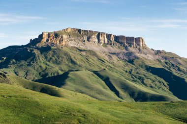 Malyi Bermamyt Dağı 'nın sarp kayalıkları ve güneşli yaz sabahında yeşil çayırlar. Karachay-Cherkessia, Kuzey Kafkasya, Rusya 'daki dağ manzarası