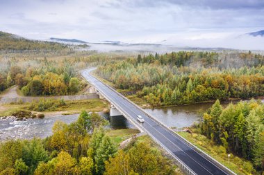 Sonbahar Taiga Ormanı 'ndaki nehir üzerindeki yol köprüsünün havadan görünüşü. Sibirya 'da sonbahar mevsimi doğa manzarası. Kultuk yakınlarındaki A-333 otoyolu, Irkutsk Oblastı, Rusya