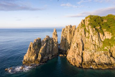 Güneş doğarken deniz kıyısında çatlakları olan dik kayalar. Gamov Yarımadası 'ndaki Babkina Burnu' nun havadan görünüşü. Primorsky Krai, Uzak Doğu, Rusya 'da deniz manzarası