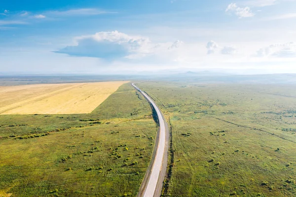 Aerial view of Trans-Siberian Highway near Chernyshevsk in Zabaykalsky Krai, Russia. Road among green flatlands and agricultural fields in a sunny weather