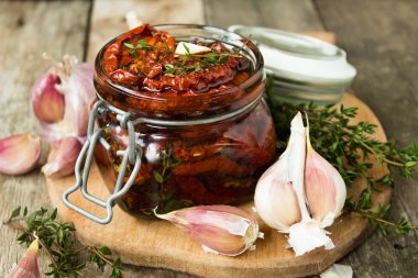 ahşap arka planda sarımsak ve biberiye ile cam kavanozda kurutulmuş domates 