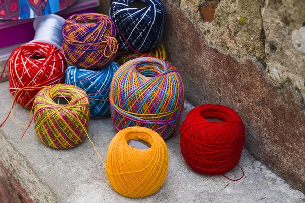Skeins of bright colored wool lie on the stone border near the w