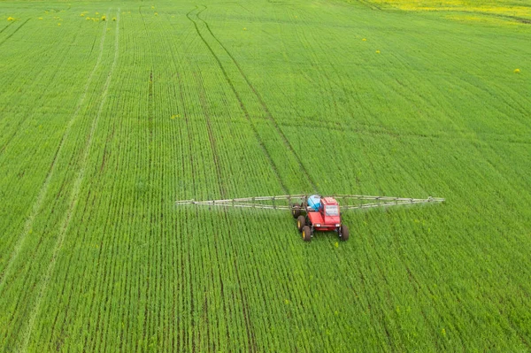 Treatment of wheat fields with herbicides. A tractor with a spray gun is walking on a green field. An aerosol trail is visible under the spray gun. Shooting from a drone. Blurred motion.