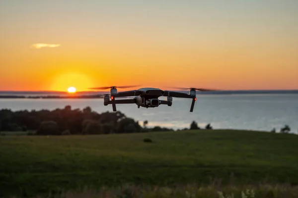 Quadrocopter in flight against the background of the river at the setting sun. The drone\'s tail lights are on. Copy space.