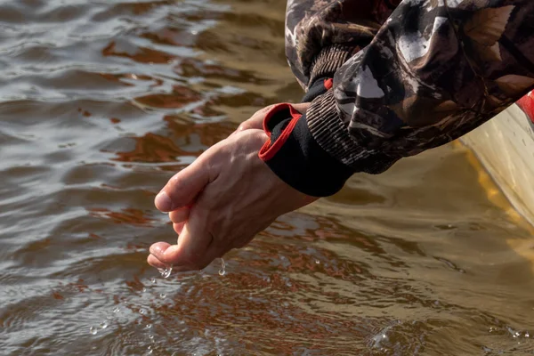 A fisherman from a boat washes his hands in the river. Men\'s hands are depicted in a camouflage jacket. water drips from my palms.