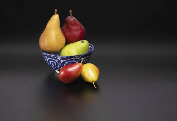 Healthy and nutritious snacks.  Delicious fresh pears on a black background with text space.  Forelle, Bosc, D'Anjou, Starkrimson Red Pears variety in a blue and white ceramic bowl.