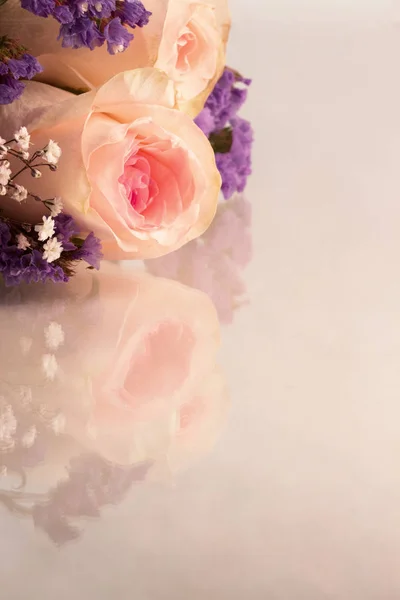 Pink roses and small lavender and white flowers on a reflective background with copy space