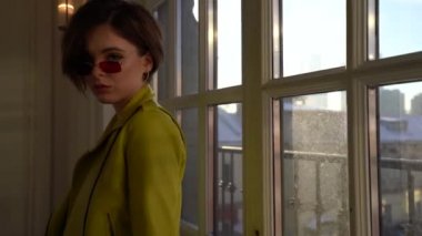 Esmer kadın güneş gözlüğü ve pencerenin yanında poz ışık yeşil deri ceket. Moda çekim