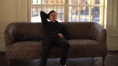 Siyah bir gömlek ve pantolon koltukta oturan bir adam fotoğrafçı saçları elleriyle, dokunmadan diyor, kanepede kalkar ve elleriyle, bir şey gösterir ileri gider