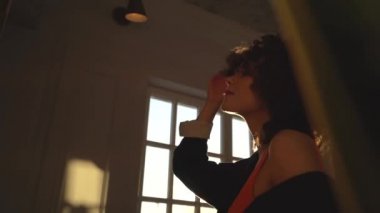 Turuncu bir beden ve bir siyah ceket siyah kıvırcık saçlı güzel bir kadın kameraya yoğurmamız standları ve güneşte gülümseyen elleriyle, saçlarını dokunur