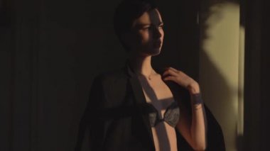 Kısa saç kesimi güzel bir kadınla siyah iç çamaşırı giymiş ve siyah bir adamın ceketi gölge ve kamera için poz duruyor