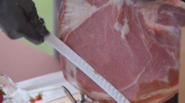 Siyah eldiven giymiş elinde bir parça jambon ya da et uzun özel bir bıçak ile kesmek.