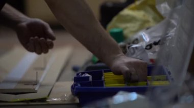 Bir adamın elini vida/cıvata mavi bir organizatör/çekmece/bavul dan ortaya çıkarır ve onları bir ahşap tahta üzerine koyar