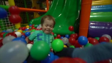 Küçük bir çocuk / çocuk turkuaz bir t-shirt giymiş ve mavi pantolonu slaytlar renkli toplar, gerçek zamanlı bir havuza yeşil slaytta aşağı doğru