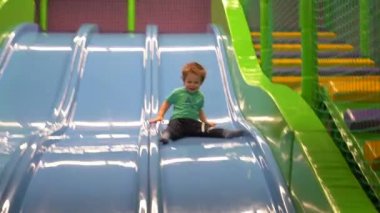 İki ya da üç yaşında bir çocuk bir turkuaz t-shirt giymiş ve koyu mavi slaytlar çocuk oyun odası mavi slaytta aşağı doğru pantolonu. Yakın çekim