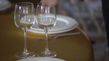 Altın bir masa örtüsü ile masada beyaz tabaklar, şarap gözlük, çatal yalan, bir kadın eli onları düzeltir