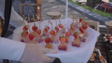 Beyaz bir gömlek ve berry sos, kızarmış peynir ve çilek olan bir tepsi ile şeffaf bardak, elinde eldiven garson bir adam aperatifler masanın üzerine koyar