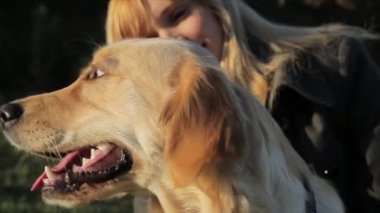 Genç bir kadın, Sarışın, bir köpek doğurmak yanında oturan Golden Retriever, kafasını okşayarak, kulakları okşamaya, gülüyor, yakın çekim