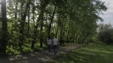 Aşıklar (erkek ve kadın) mavi kot pantolon ve beyaz t-shirt giymiş, eller tutarak, sarılma, kumlu bir yolda yürüyüş, arka çekim, yaz/bahar güneşli gün