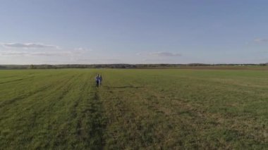 Mavi gömlekli ve kot pantolongiyen bir adam mavi elbiseli bir kızın elini tutar, sahaya çıkarlar ve sonra kameraya koşmaya başlarlar, güneşli bir yaz gününde hava fotoğrafçılığı.