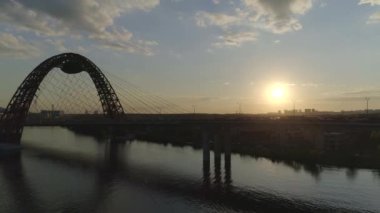 Hava/drone fotoğrafçılığı: güneş batımında nehir üzerinde kırmızı metal kemer ile kablo-kaldı araba Köprüsü, ağır trafik, kamera köprüye yaklaşıyor