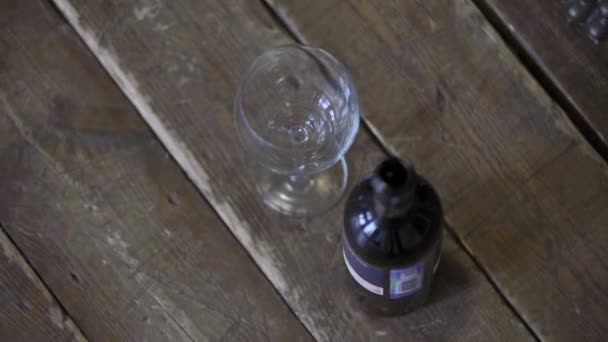 木製の床にワインの空のガラスとワインのボトルである 女性の手は ガラスを取るとフレームから削除し クローズアップ — ストック動画