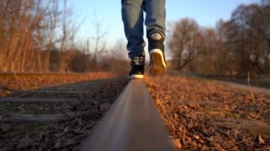 Altın spor ayakkabı, mavi kot pantolon ve mavi ceket ile siyah giymiş kız ilk bir bacak koyar, sonra raylı ikinci bacak ve kamera uzak gitmeye başlar, ilkbahar / sonbaharda gün batımında çekim